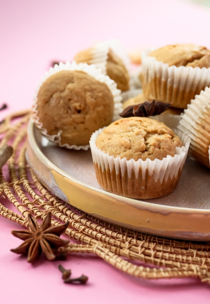 Golden mini banana muffins on decorative plate with spices