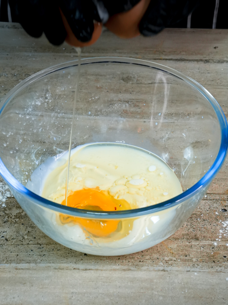 Adding an egg to wet ingredients for cinnamon muffins in a glass mixing bowl