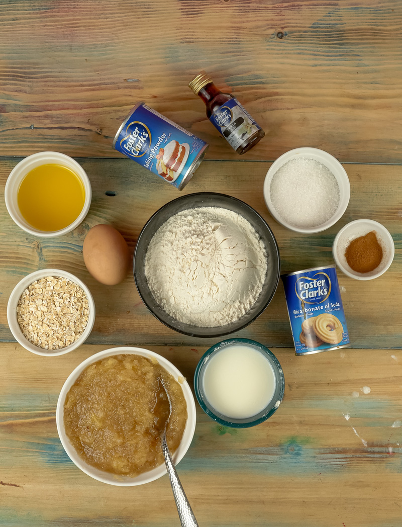 Applesauce muffin ingredients on wooden surface including flour, oats, and baking powder