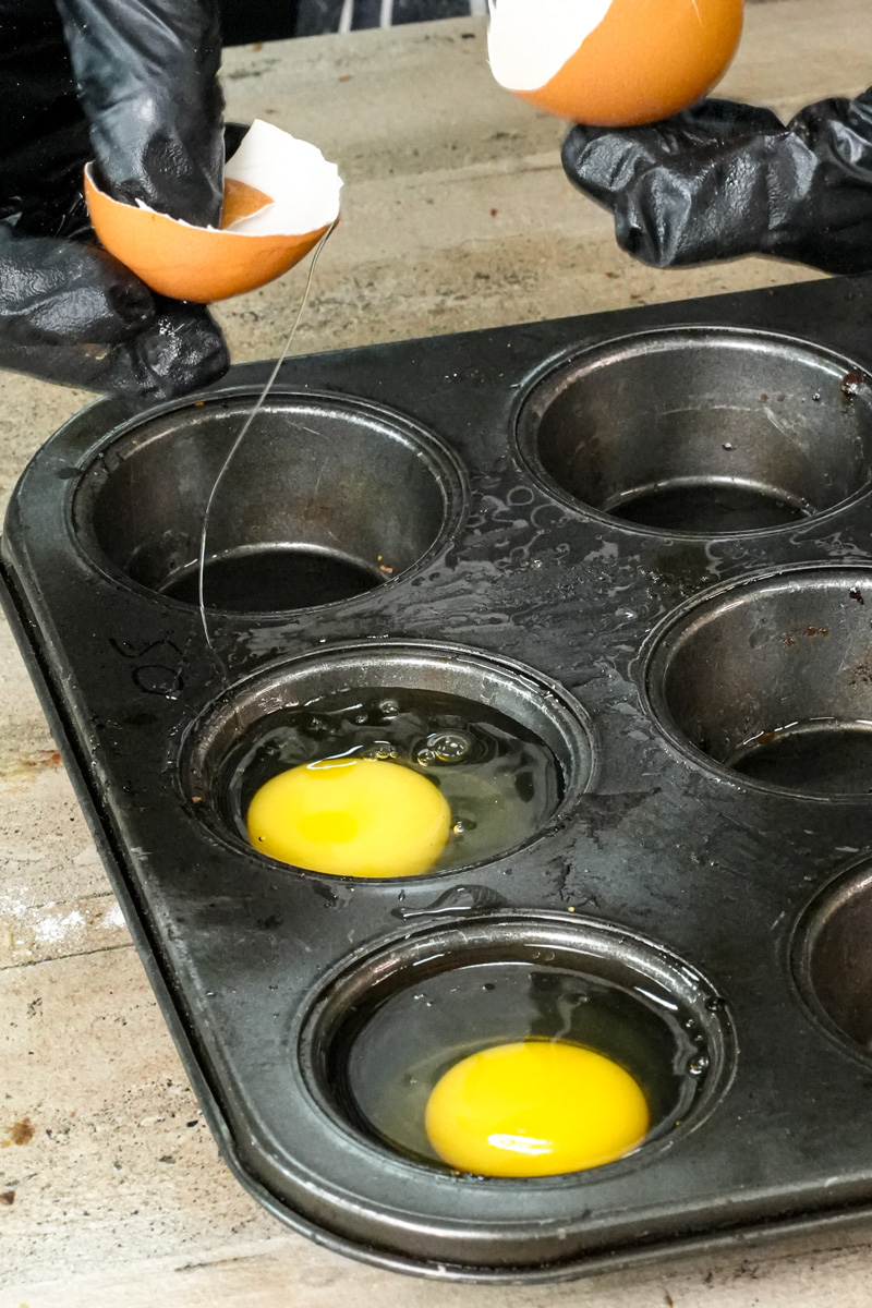 Cracking fresh egg into muffin tin with black gloves