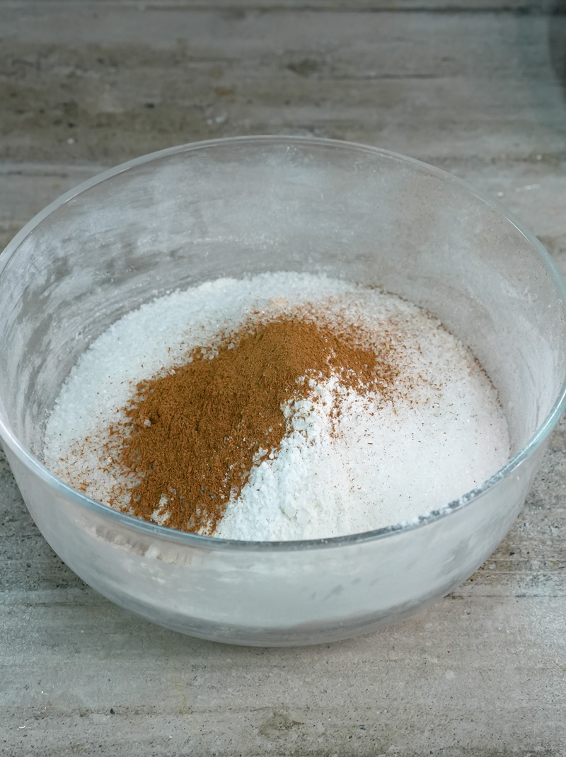 Dry ingredients for cinnamon muffins, including flour, sugar, and cinnamon, in a glass mixing bowl