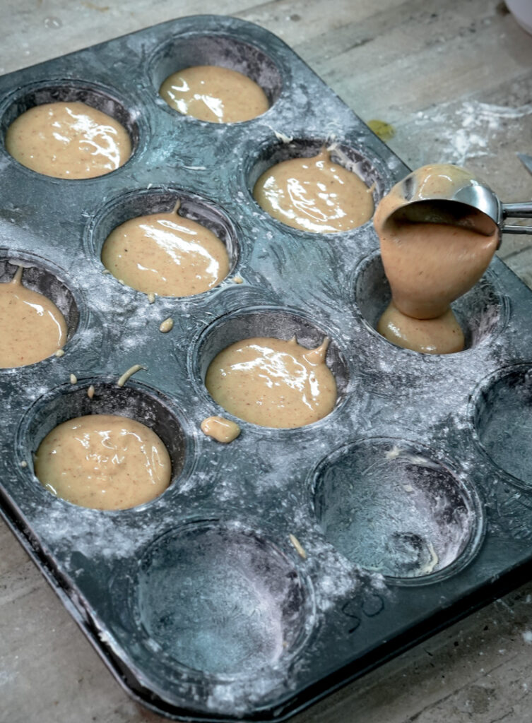 Filling a floured muffin tin with cinnamon muffin batter