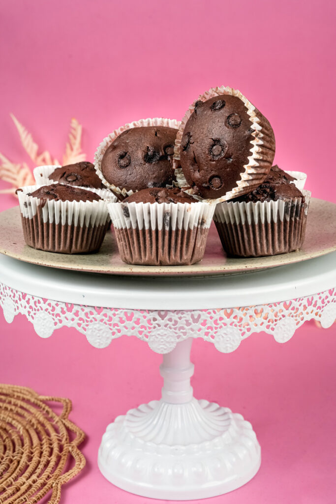 Freshly baked double chocolate muffins on white cake stand with pink background