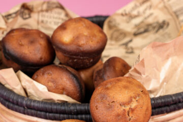 Close-up of a wicker basket filled with freshly baked cinnamon muffins, with decorative paper and dried foliage, on a pink background