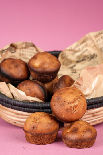 Close-up of a wicker basket filled with freshly baked cinnamon muffins, with decorative paper and dried foliage, on a pink background