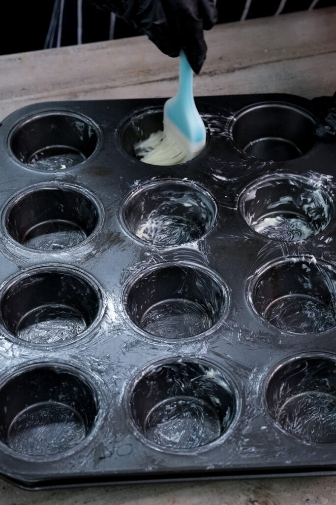 Greasing a muffin tin with butter using a pastry brush for cinnamon muffins