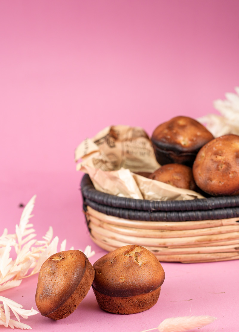 Homemade cinnamon muffins, with two in the foreground and a basket of muffins behind, styled with dried foliage