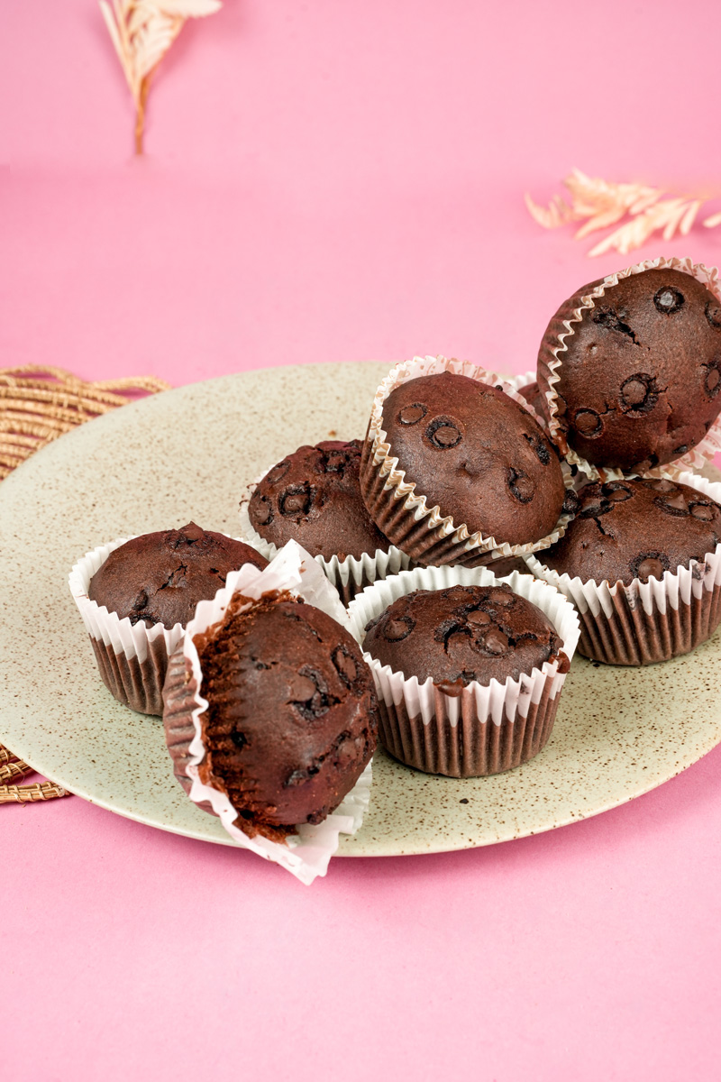 Homemade double chocolate muffins on speckled plate against pink backdrop