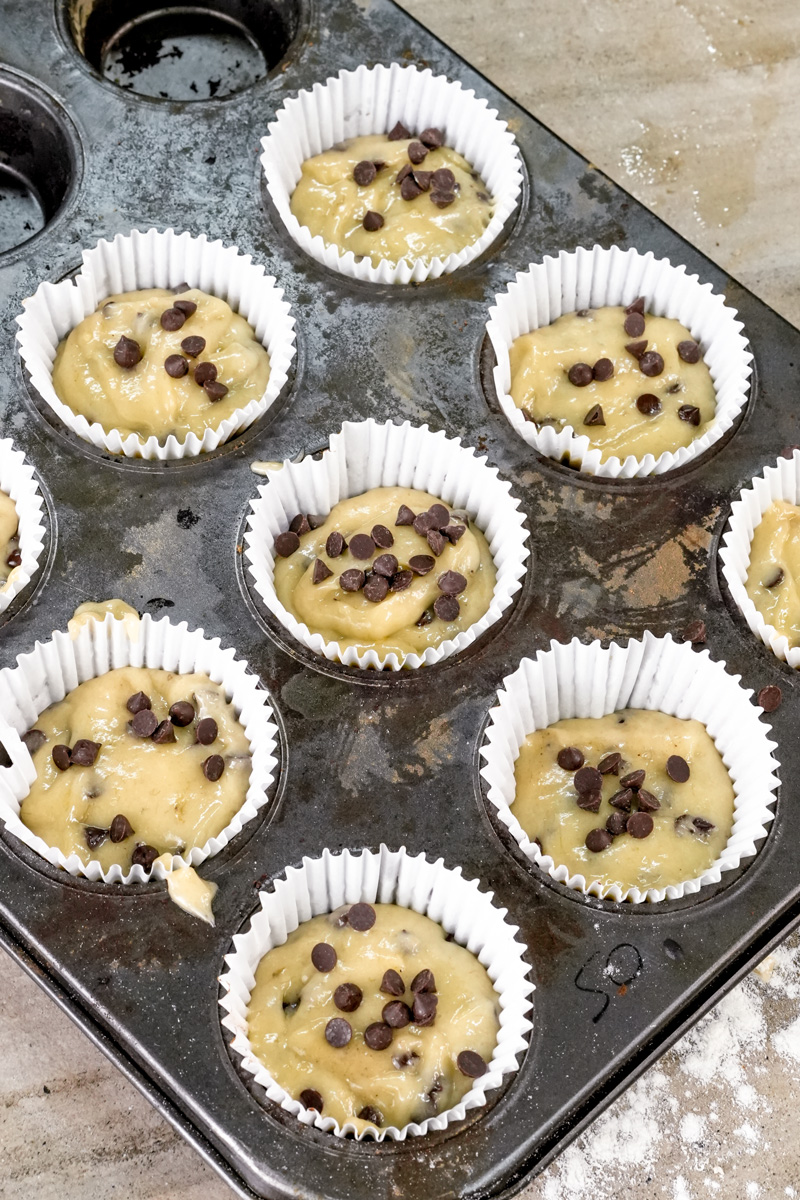 Muffin tin filled with banana chocolate chip batter with extra chips on top