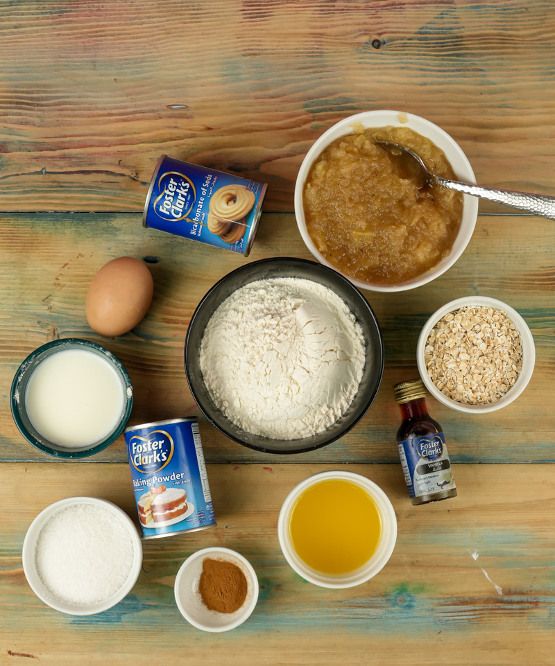 Oatmeal muffin ingredients on wooden surface including flour, oats, eggs and milk