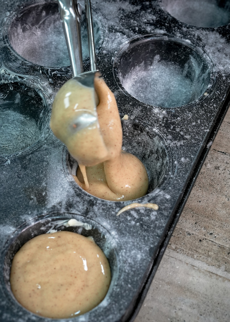 Pouring cinnamon muffin batter into a floured muffin tin cup with a spoon