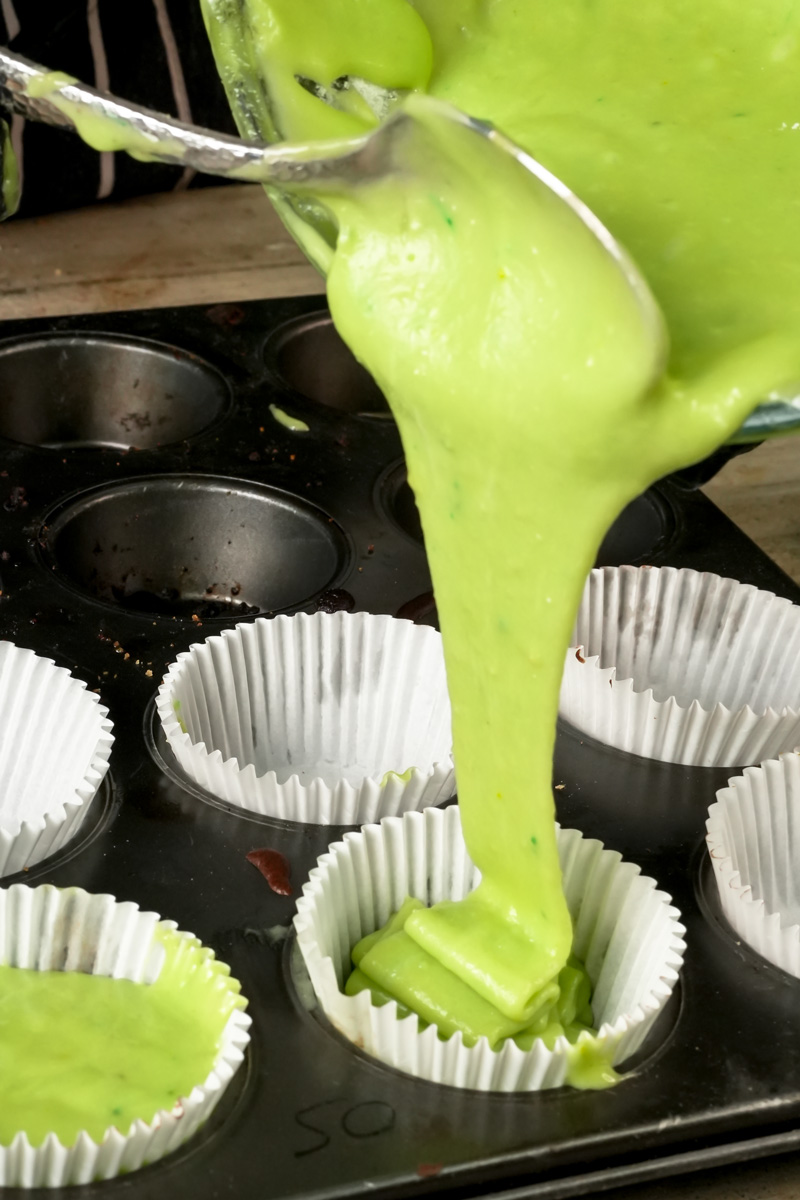 Pouring green pistachio muffin batter into paper liner