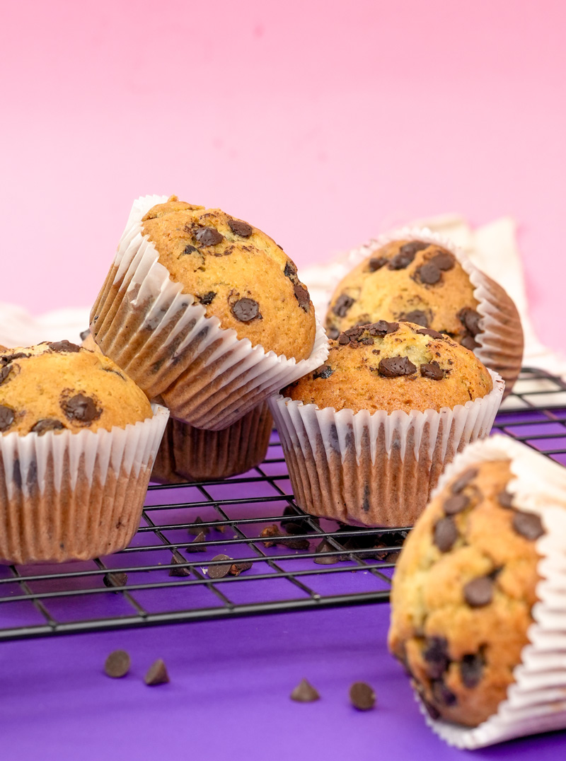 Scattered banana protein muffins with chocolate chips on a cooling rack.
