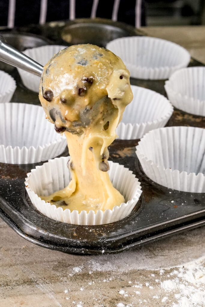 Scooping banana chocolate chip muffin batter into liner