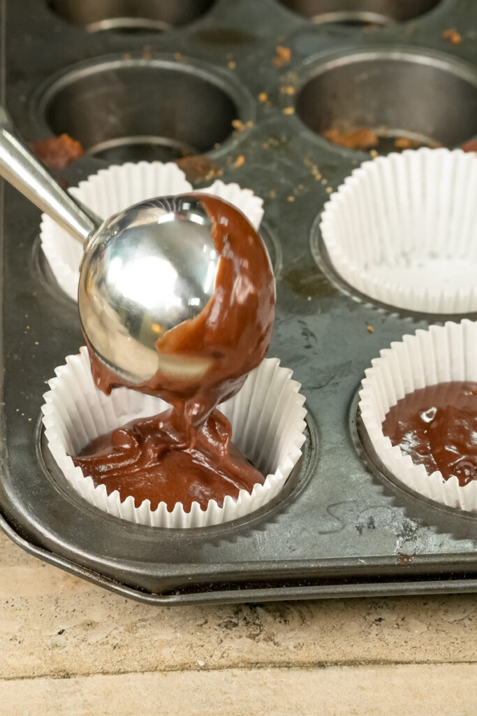 Scooping chocolate muffin batter into lined muffin tin