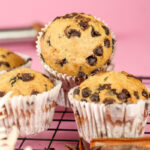 Freshly baked banana chocolate chip muffins on cooling rack against pink background
