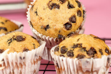 Freshly baked banana chocolate chip muffins on cooling rack against pink background