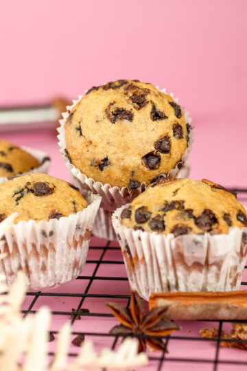 Freshly baked banana chocolate chip muffins on cooling rack against pink background