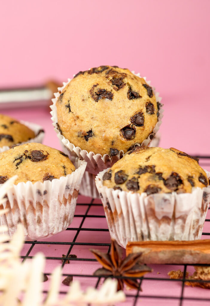 Freshly baked banana chocolate chip muffins on cooling rack against pink background