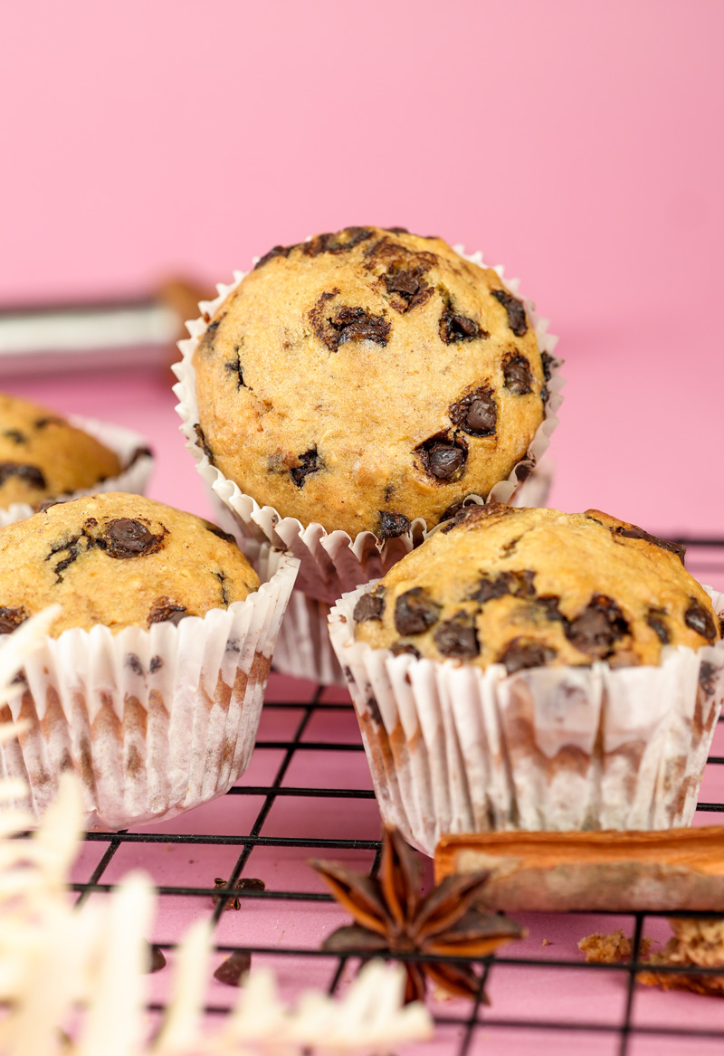 Freshly baked banana chocolate chip muffins on cooling rack against pink background