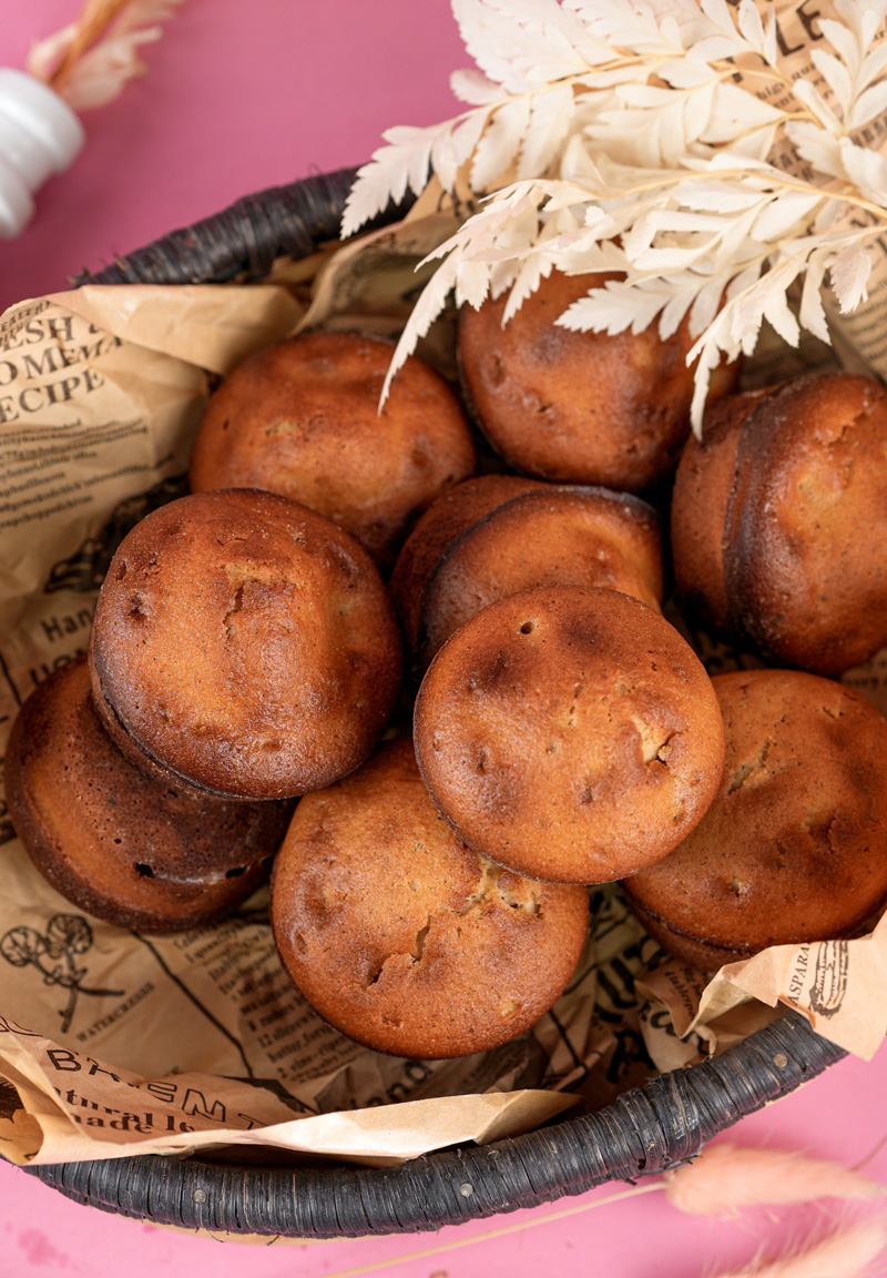 Basket of freshly baked cinnamon muffins with decorative paper and dried white foliage on a pink surface