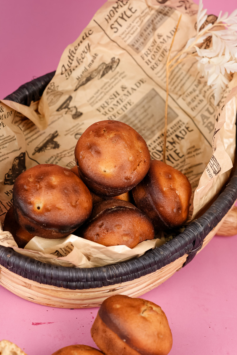 Close-up of a wicker basket filled with freshly baked cinnamon muffins, with decorative paper and dried foliage, on a pink background