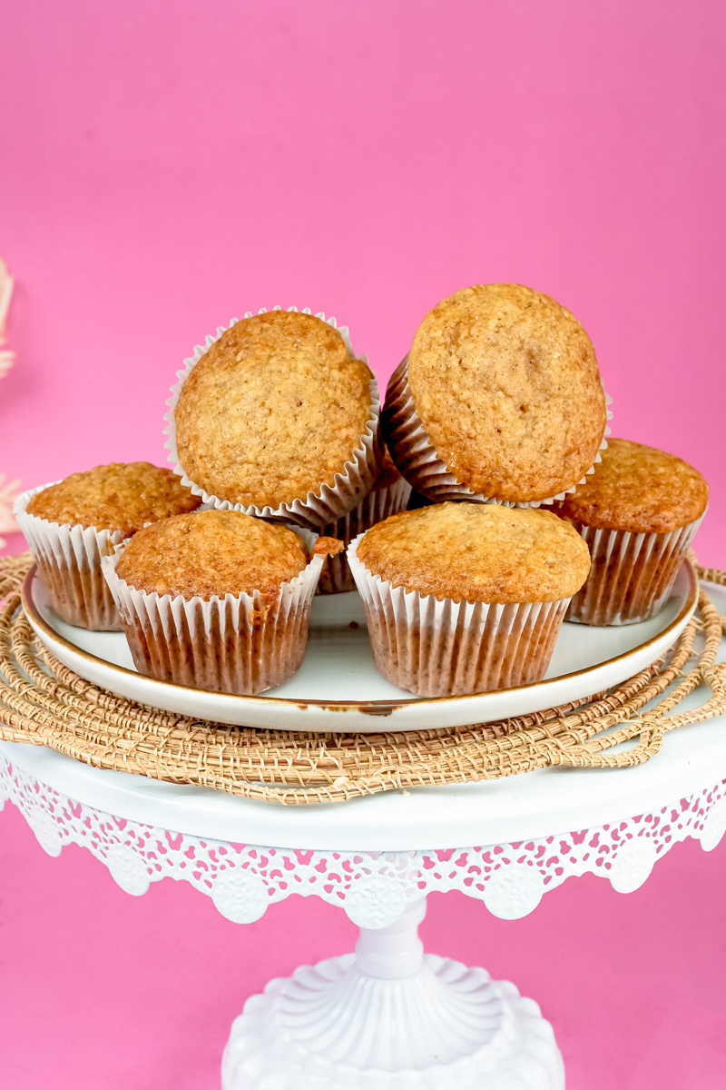 Golden applesauce muffins stacked against pink background