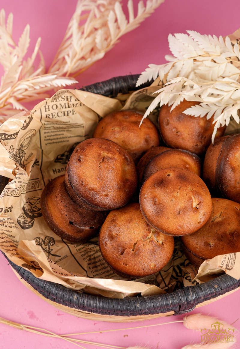 Overhead view of homemade cinnamon muffins in a paper-lined wicker basket with dried foliage
