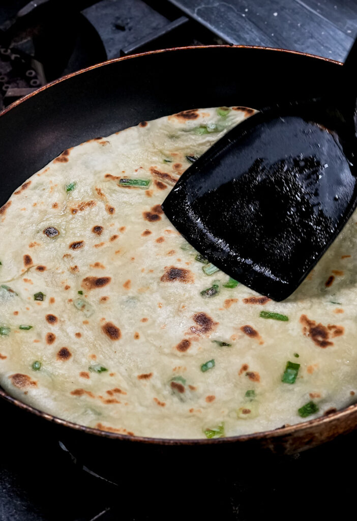 Pressing Chinese scallion pancake while cooking with spatula