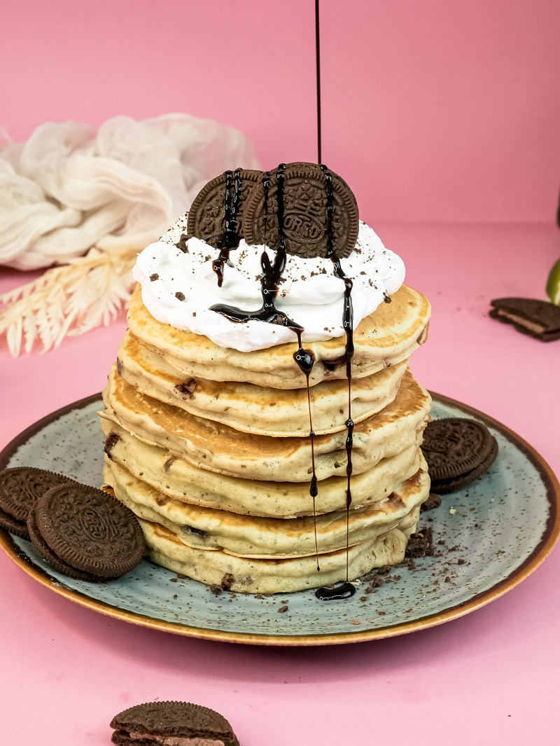 Chocolate syrup being poured over Oreo pancake stack with whipped cream