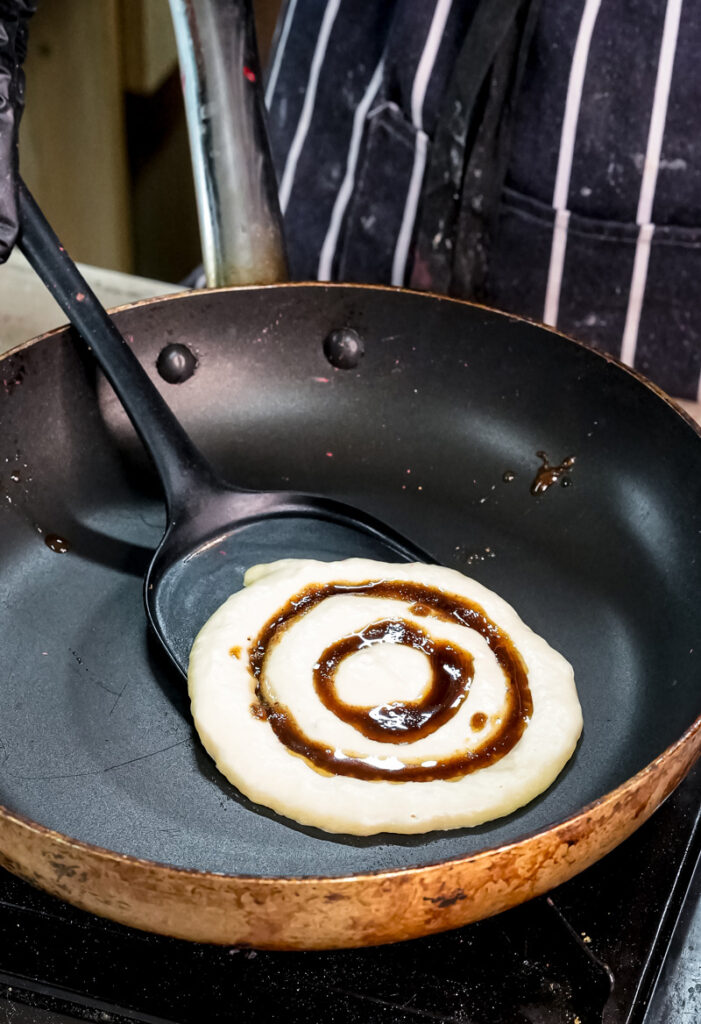 Cinnamon roll pancake cooking in pan showing spiral design