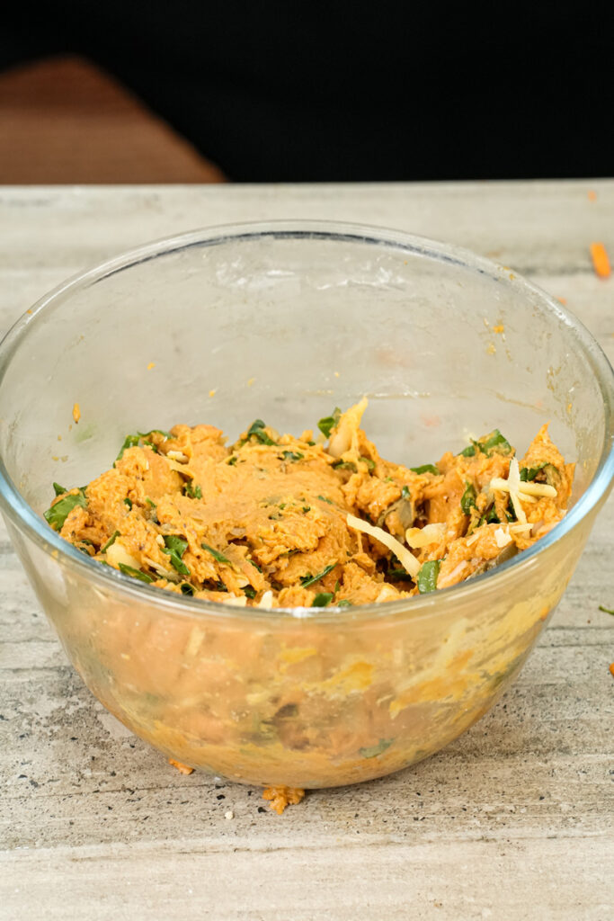 Combining pizza muffin ingredients with wooden spoon in glass bowl