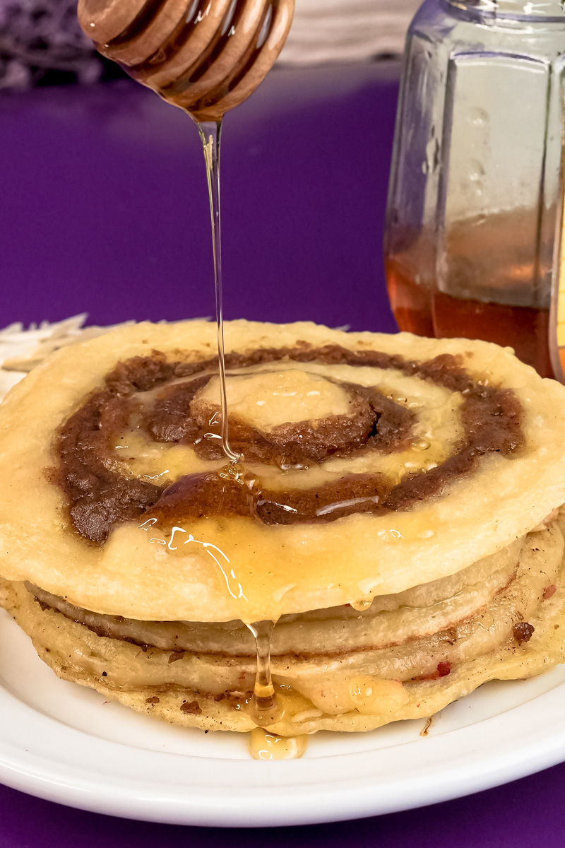Drizzling honey on cinnamon roll pancakes with wooden honey dipper