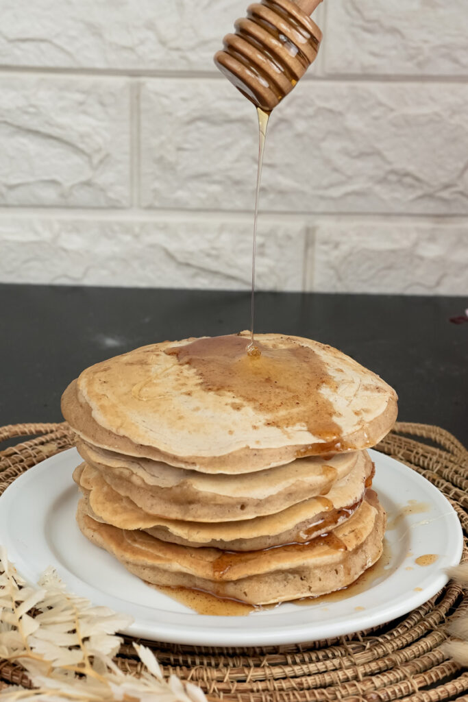 Drizzling honey over whole wheat pancakes with wooden honey dipper
