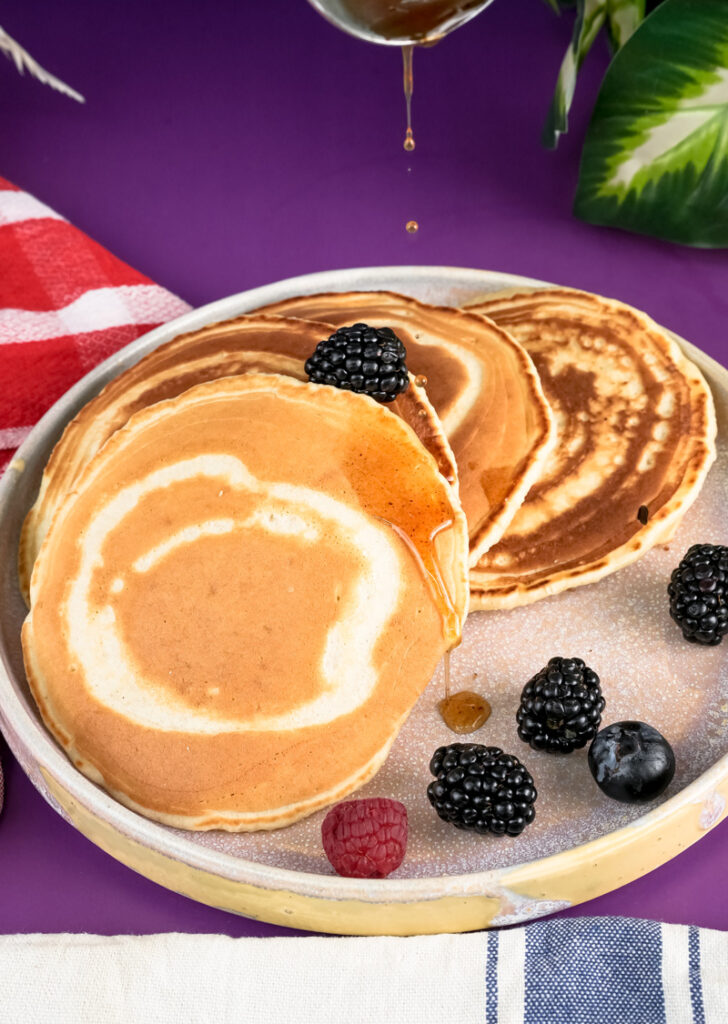 Drizzling syrup over silver dollar pancakes with blackberries and raspberries