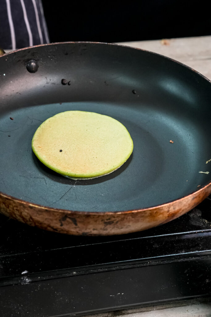 Flipped green banana spinach pancake cooking in pan