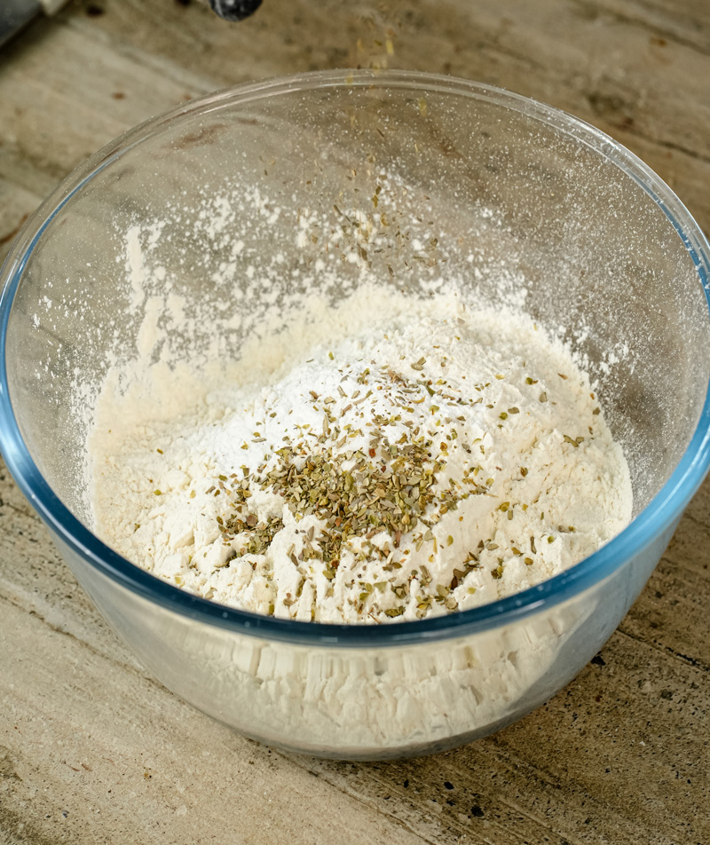 Flour and herbs mixed in glass bowl for pizza muffins