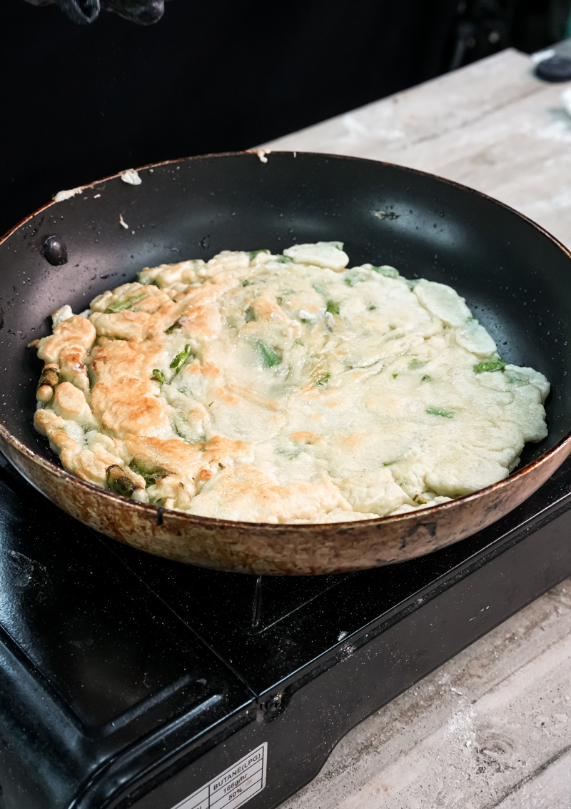Golden brown Korean scallion pancake cooking in skillet