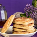 Golden gluten-free pancakes stacked on plate with purple background