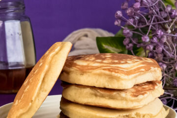 Golden gluten-free pancakes stacked on plate with purple background