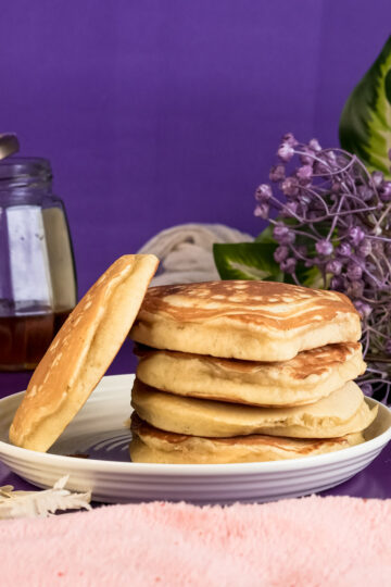 Golden gluten-free pancakes stacked on plate with purple background
