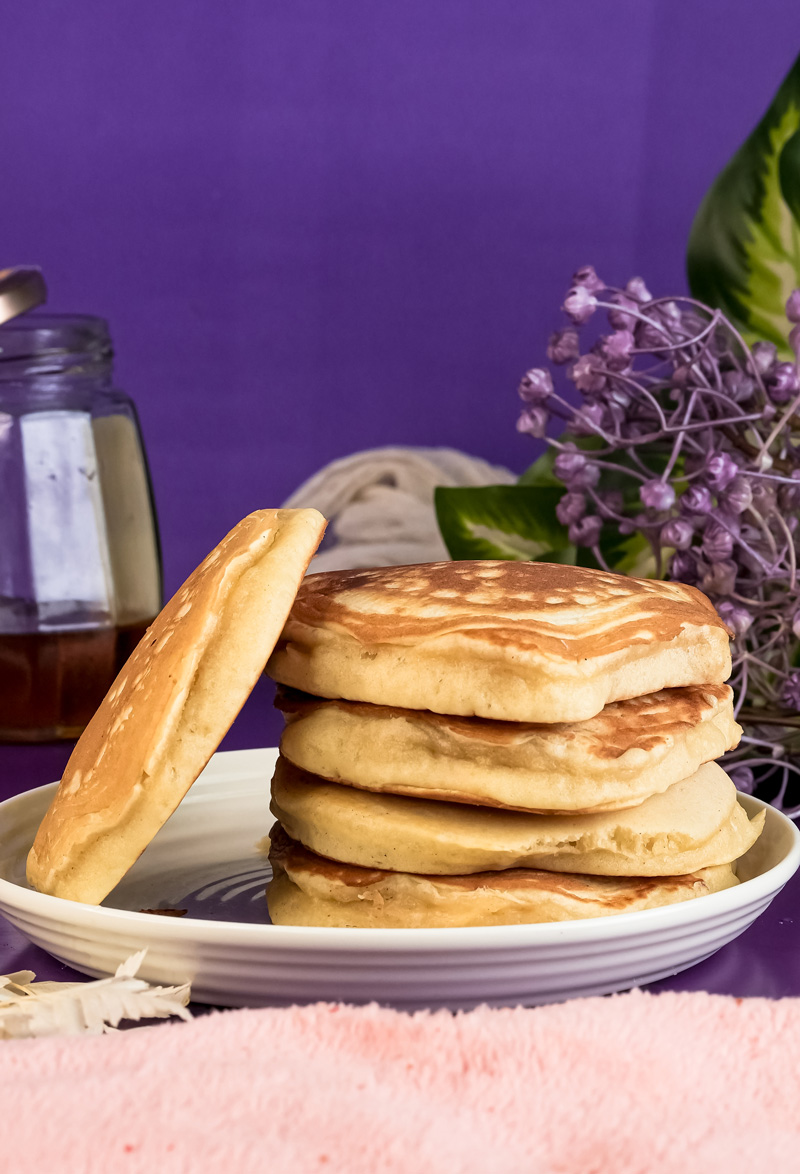 Golden gluten-free pancakes stacked on plate with purple background