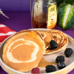 Honey being drizzled on silver dollar pancakes with wooden dipper