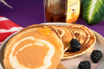 Honey being drizzled on silver dollar pancakes with wooden dipper