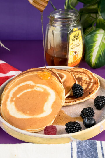 Honey being drizzled on silver dollar pancakes with wooden dipper