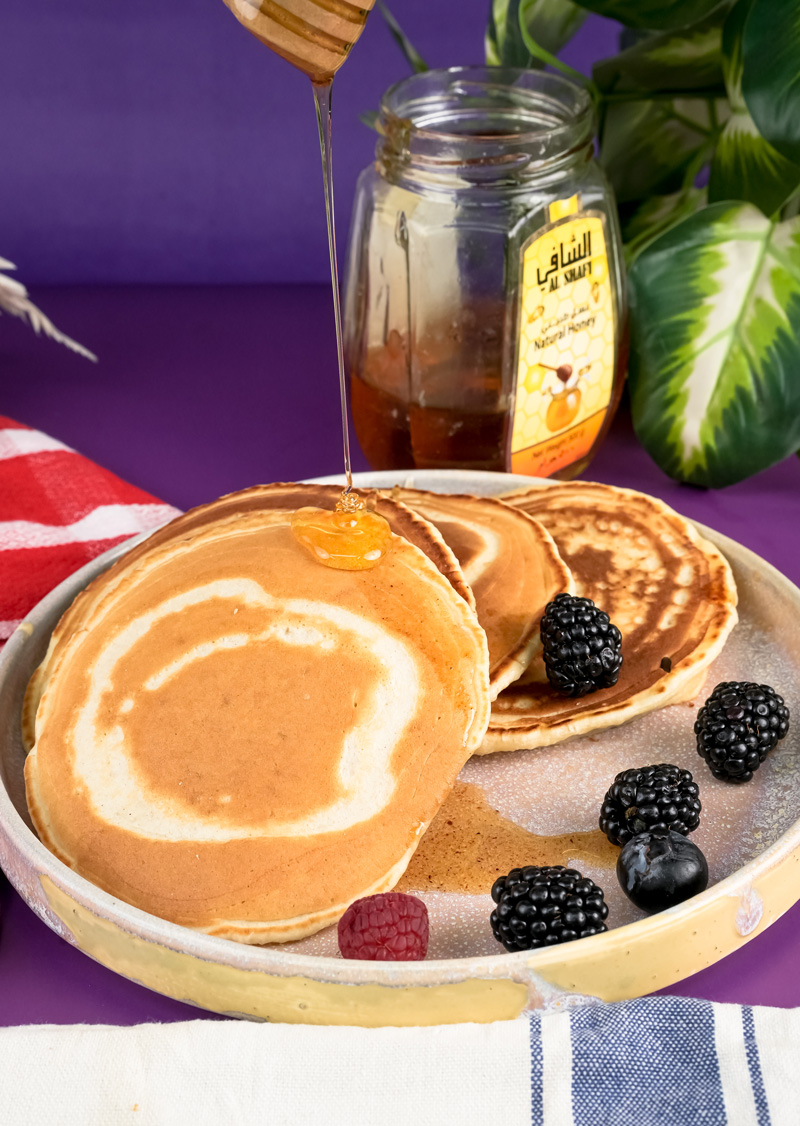 Honey being drizzled on silver dollar pancakes with wooden dipper