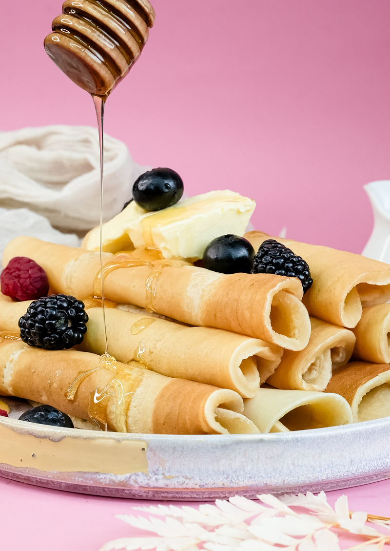 Drizzling honey over pancake rolls with berries