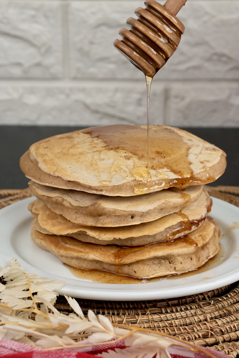 Honey being poured onto stack of whole wheat pancakes