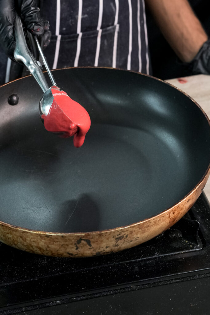 Ladling red velvet pancake batter into non-stick pan