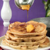 Maple syrup being poured over apple cinnamon pancakes with butter